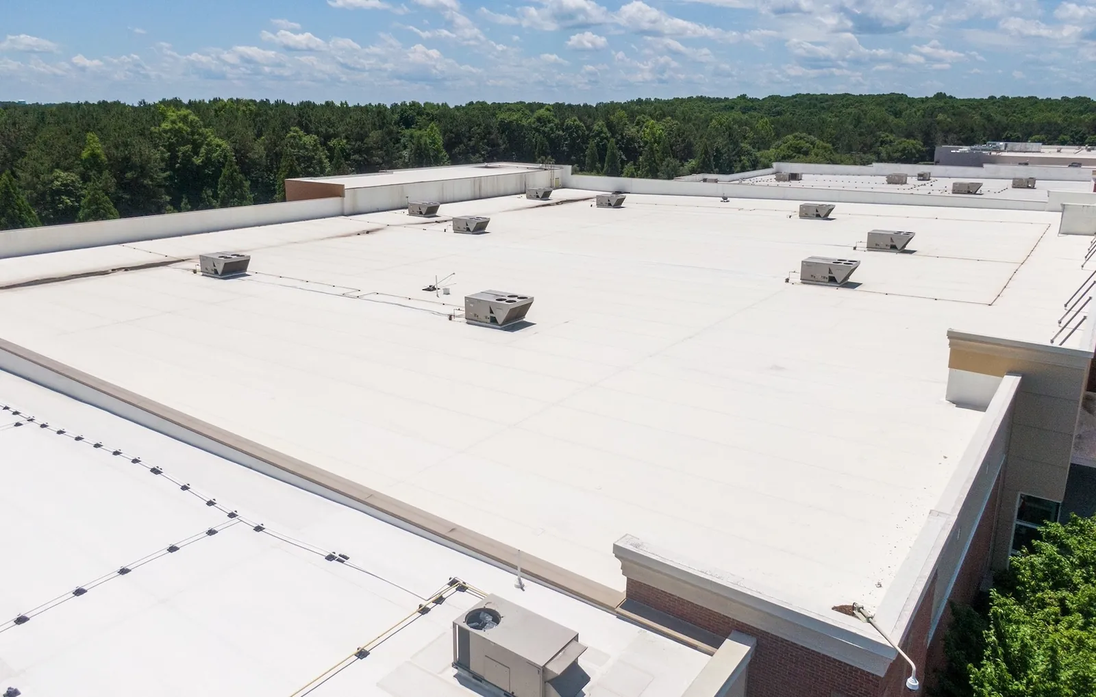 White low-slope membrane roof showing broad drainage fields and rooftop penetrations