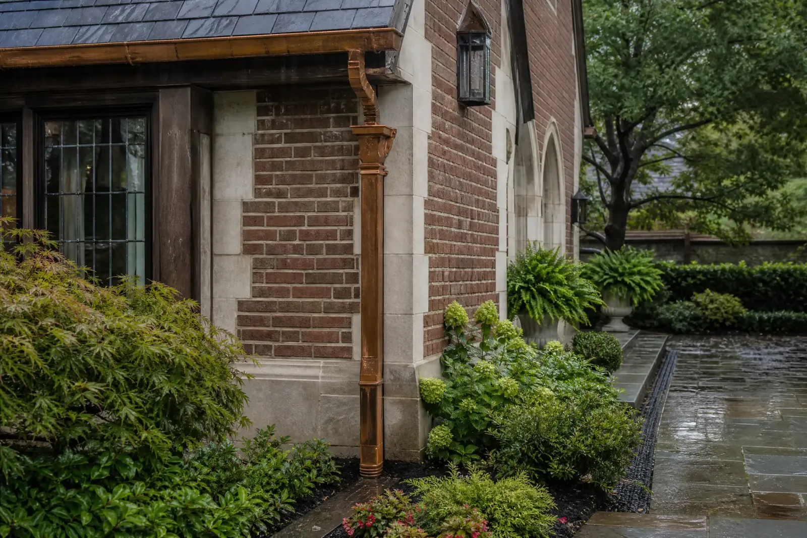 Copper downspout and gutter system carrying roof water beside a masonry facade